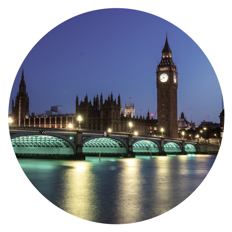 Night view of London’s Big Ben and the Houses of Parliament, with Westminster Bridge crossing the River Thames, illuminated by city lights—Cority and Greenstone tones reflecting softly in the water.