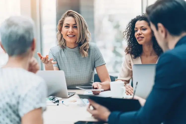 Four professionals sit around a table in a bright office, engaged in discussion.